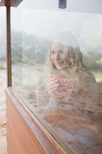 Femme de contenu réfléchie avec une tasse de café regardant par la fenêtre