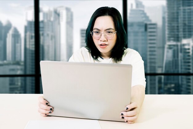 Une femme contrariée utilisant un ordinateur portable sur le bureau avec un ordinateur portatif dans un bureau