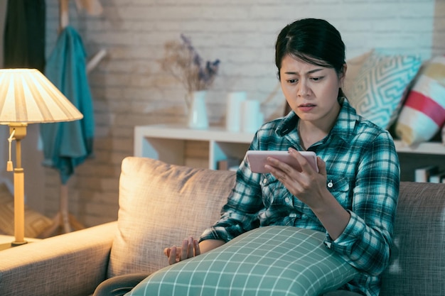 femme coréenne asiatique bouleversée regardant du contenu en ligne sur un smartphone assis sur un canapé dans un salon sombre à la maison la nuit. fille triste regarder un film d'amour romantique film misérable sur téléphone portable en fronçant les sourcils.