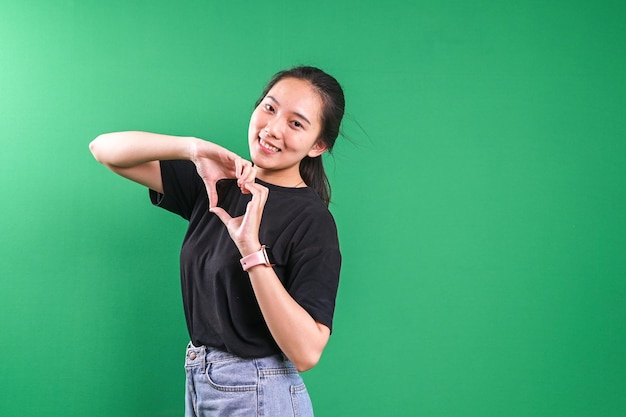 Une femme coréenne attrayante se sent heureuse et romantique en faisant des gestes en forme de cœur sur un fond vert