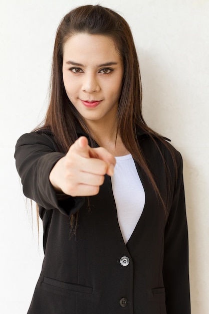 Femme en costume d'affaires main pointant vers l'avant avec une expression de visage souriant amical