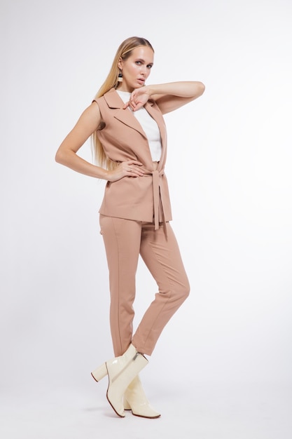 Femme en costume beige pantalon gilet bottes posant sur fond blanc Studio Shot portrait Blonde