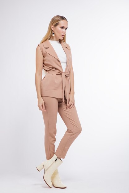 Femme en costume beige pantalon gilet bottes posant sur fond blanc Studio Shot portrait Blonde