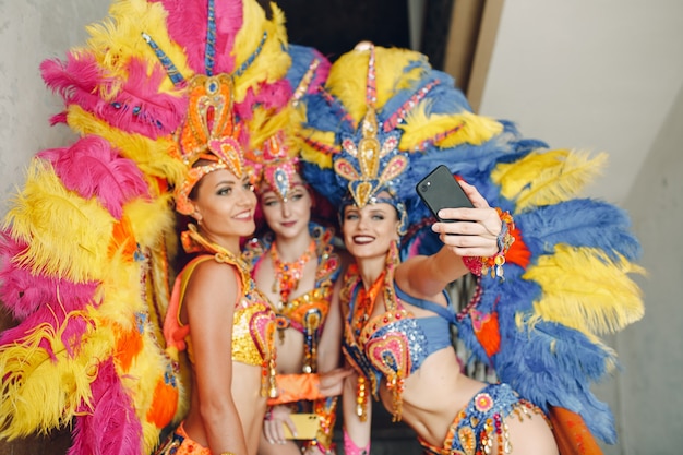 Une femme en costume de carnaval de samba brésilienne avec un plumage de plumes colorées avec un téléphone portable prend un selfie dans l'ancienne entrée avec une grande fenêtre.