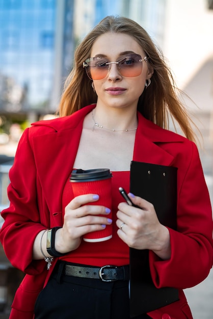 Femme en costume formel profitant d'une journée ensoleillée et marchant près des gratte-ciel pendant