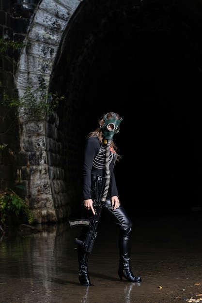 Une femme en costume noir et masque à gaz avec une mitrailleuse dans les mains