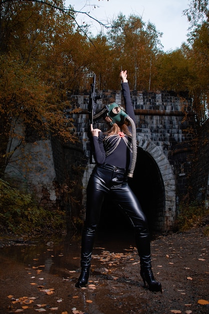 Photo une femme en costume noir et masque à gaz avec une mitrailleuse dans ses mains.