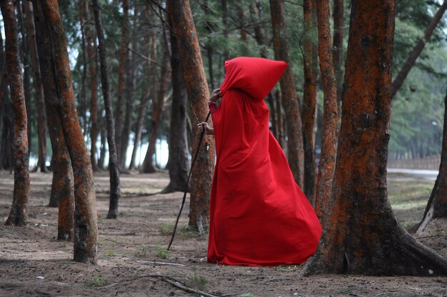 Photo femme en costume rouge marchant au milieu des arbres dans la forêt