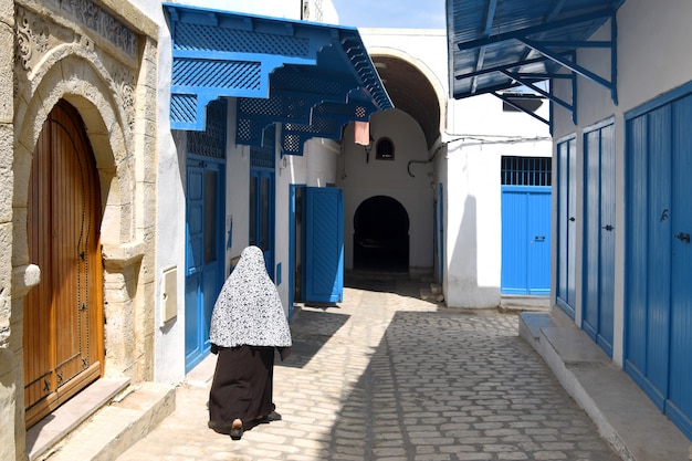 Photo femme en costume traditionnel se promène le long d'une rue étroite de la vieille ville de sousse en tunisie