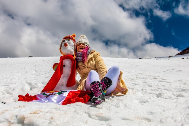 Femme à côté d'un bonhomme de neige et d'un drapeau péruvien au sommet d'une montagne enneigée au Pérou