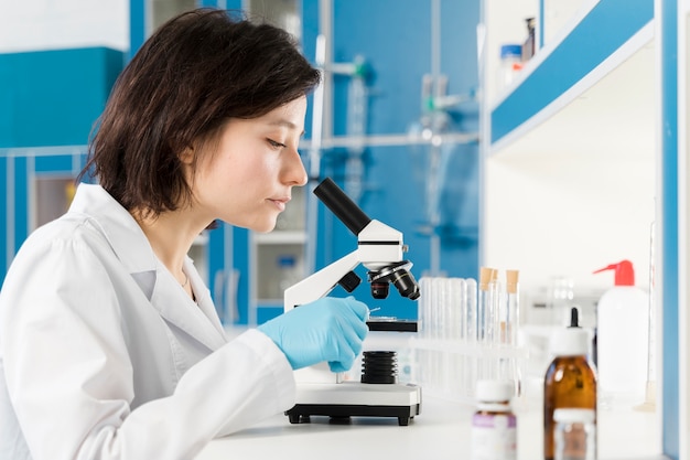 Femme de côté regardant à travers un microscope