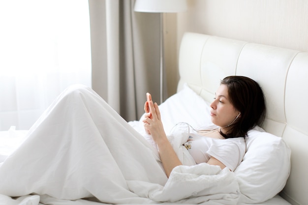 La Femme Couchée Dans Son Lit Avec Le Téléphone Et écouter De La Musique