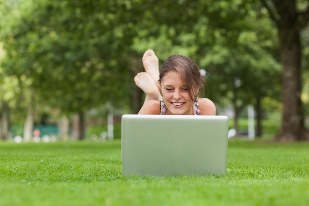 Femme couchée sur l&#39;herbe et en utilisant un ordinateur portable dans le parc