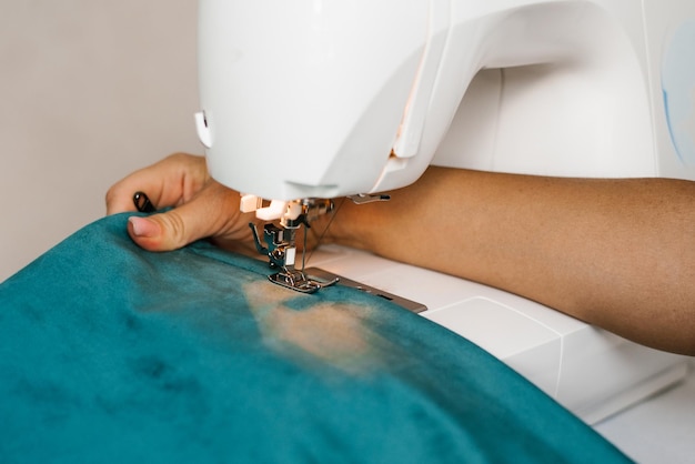 Une femme coud du tissu turquoise sur une machine à coudre