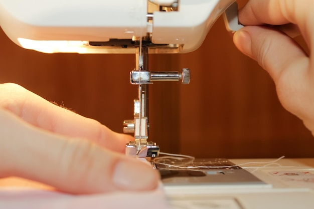 Une femme coud sur une machine à coudre électrique blanche. Le concept de couture, de coupe, de travaux d'aiguille.