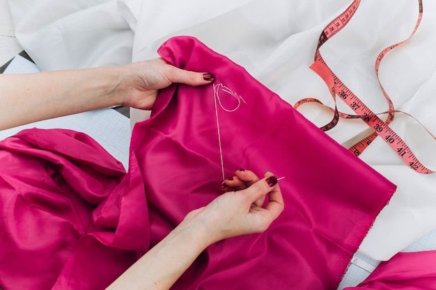 Femme coud un tissu rose foncé sur la table