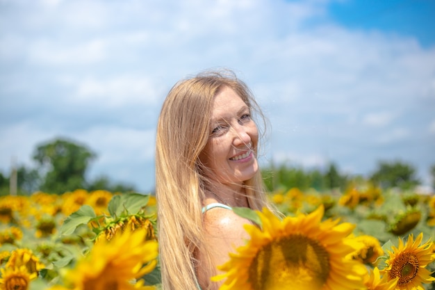 Femme à la couleur des cheveux dorés souriant dans un champ avec des fleurs de tournesol