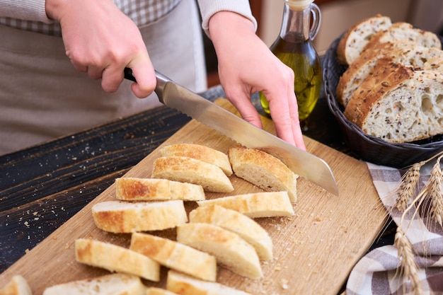 Femme coupant du pain frais à la table de cuisine en bois