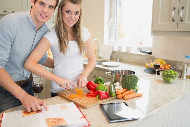 Femme coupant les légumes avec un homme lisant le livre de cuisine