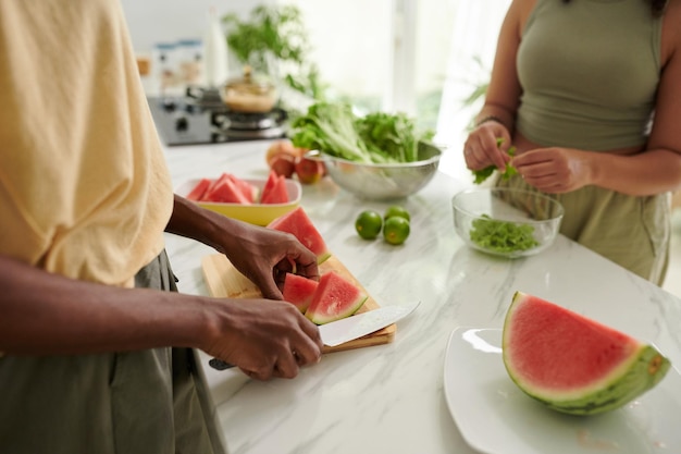 Femme coupant une pastèque quand un ami prépare une salade