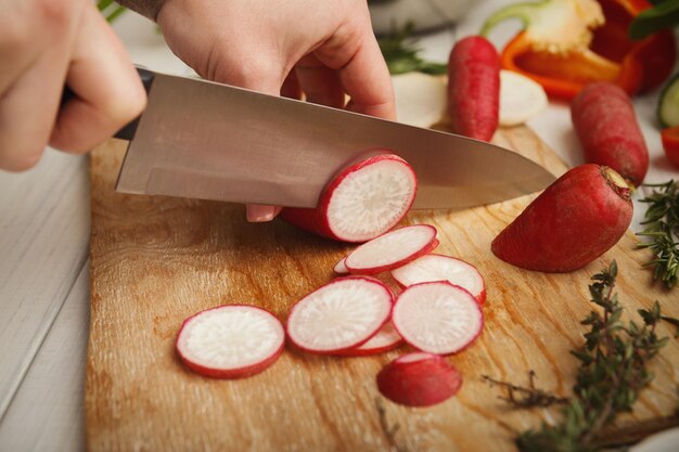 Femme coupant le radis frais sur planche de bois. Alimentation naturelle, préparation d'une salade de légumes diététique saine à la cuisine, gros plan