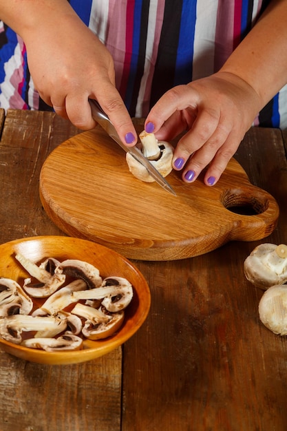 Une femme coupe des champignons champignon avec un couteau sur une planche de bois