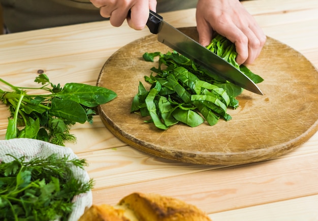 Une femme coupe des épinards sur une planche de cuisine.