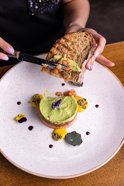 Une femme coupe un morceau de pain avec un avocat dessus.