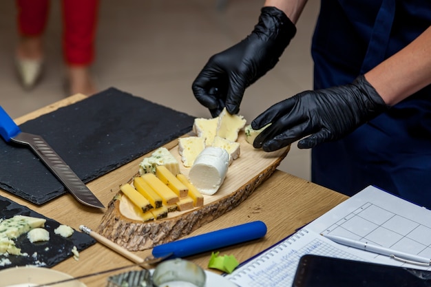 Une femme coupe des morceaux de fromage avec un couteau sur une plaque jaune pour la présentation