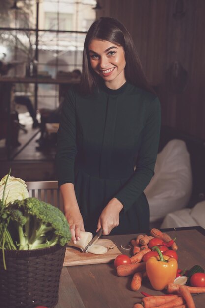 La femme coupe un oignon avec le couteau à la table en bois