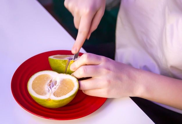 La femme coupe le pamplemousse mûr frais avec un couteau de cuisine