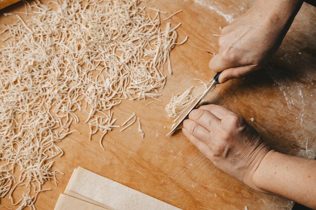 Une femme coupe la pâte avec un couteau et fait des nouilles maison dans la cuisine. Pâtes faites maison, par les mains d'une femme.