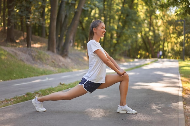 Femme coureuse qui s'étend des jambes avant d'exercer le matin du parc d'été