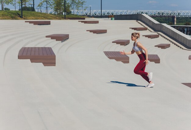 Femme en cours d'exécution Coureur fait du jogging au lever du soleil Modèle de fitness féminin s'entraînant à l'extérieur de la ville sur un quai Mode de vie sportif