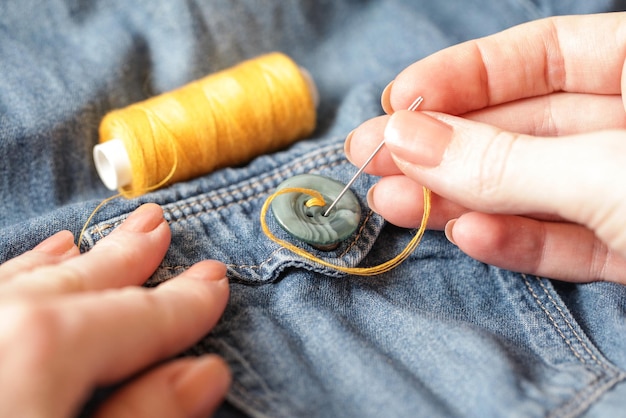 Femme cousant sur bouton fil aiguille couture bouton Jeans gros plan mode de vie authentique fait à la main