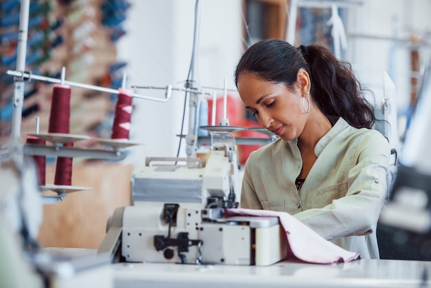 Une femme couturière coud des vêtements sur une machine à coudre en usine.