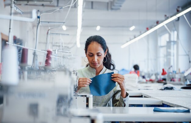 Une femme couturière coud des vêtements sur une machine à coudre en usine.