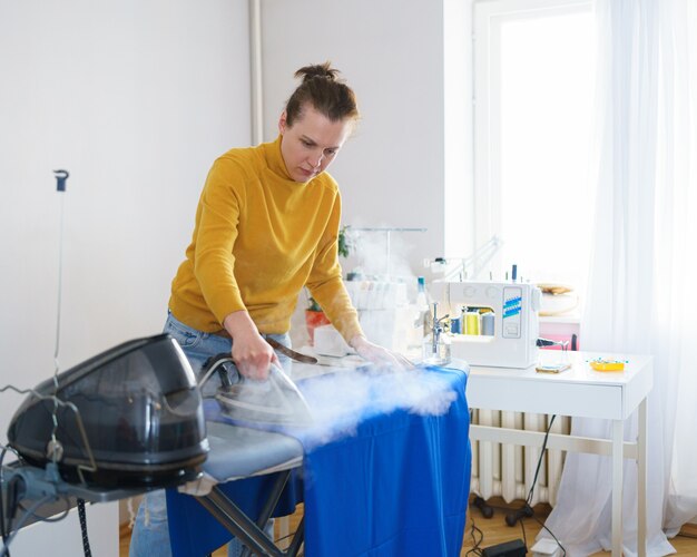 Femme couturière ou femme au foyer repassant le tissu avant de coudre tout en travaillant sur son lieu de travail