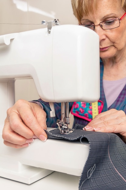 Femme de couturière senior travaillant avec un vêtement sur une machine à coudre