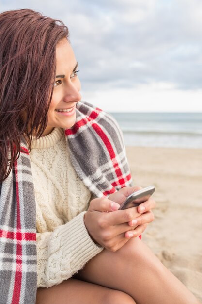 Femme couverte de couverture avec téléphone portable à la plage