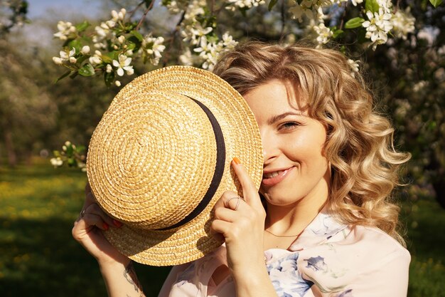 Femme couverte de la moitié du visage avec un chapeau de paille - temps heureux dans le jardin vert - printemps et été