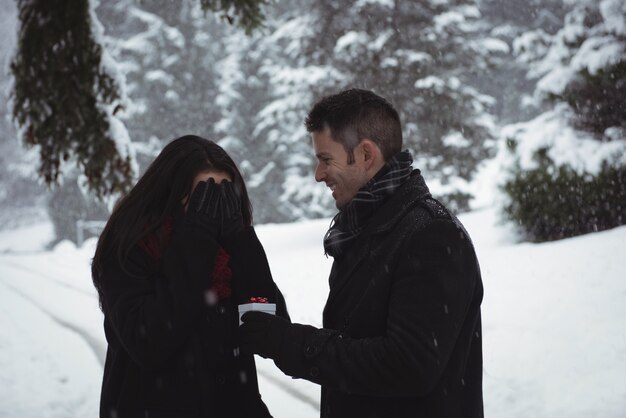 Femme couvrant ses yeux tandis que l'homme donnant un cadeau surprise en forêt pendant l'hiver