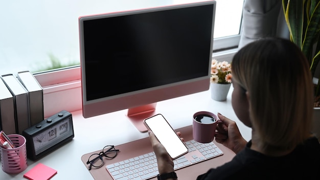 Femme créative buvant du café et utilisant un téléphone intelligent dans son espace de travail