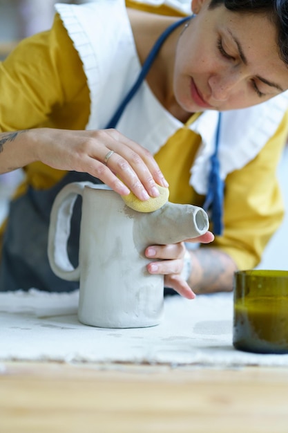 Femme créative verseuse d'argile de moulage en studio artiste féminine avec tatouages travailler sur la poterie en atelier