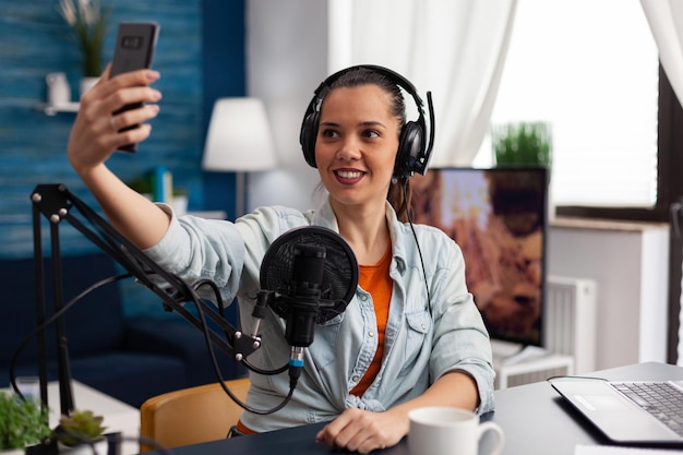 Femme créatrice de contenu utilisant un casque et un microphone pour diffuser un podcast vidéo en direct sur un smartphone. Influenceur des médias sociaux enregistrant une diffusion en ligne avec un téléphone portable dans un home studio.