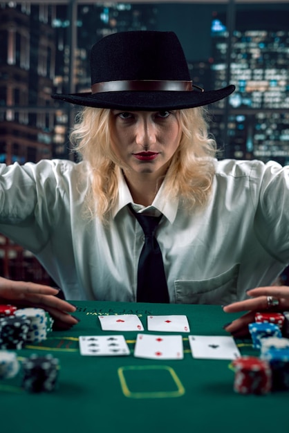 Femme croupier au chapeau avec des cartes à jouer et des jetons de poker au casino en regardant le jeu