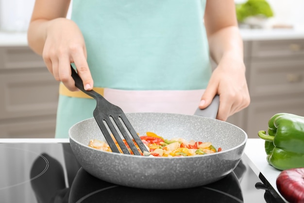 Femme cuisinant des légumes dans une poêle à frire sur la cuisinière