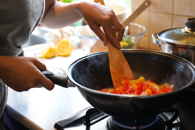 Femme cuisinant des légumes dans une poêle à frire à l'intérieur en gros plan