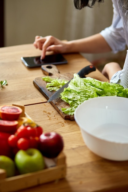 Une femme cuisine dans la cuisine à la maison, à l'aide d'une tablette numérique ou d'un smartphone, cherche une recette, un concept d'alimentation saine, végétalien ou diététique.