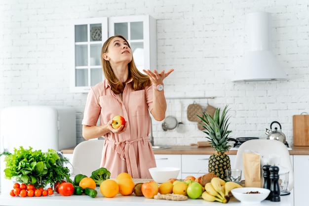 Femme en cuisine prête à préparer un repas avec des légumes et des fruits.